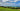 a lush green field next to the ocean under a cloudy blue sky