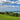 a lush green field next to the ocean under a cloudy blue sky